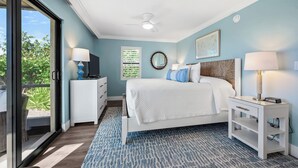 A bedroom with a bed, a television on a nightstand, a ceiling fan, and a view through a glass door.
