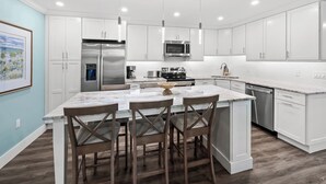 A modern kitchen with white cabinetry, stainless steel appliances, a marble island, and pendant lighting.