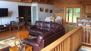 A spacious living area with a leather sofa, wooden furniture, and a TV mounted on the wall. - Mountain Cabin,Pet-Friendly,Views,HotTub,Deck,WiFi (Ferguson)