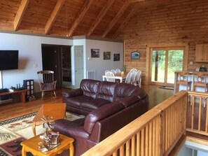 A spacious living area with a leather sofa, wooden furniture, and a TV mounted on the wall.