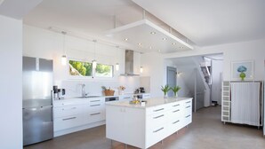 A modern kitchen with white cabinetry, a central island, and a view of greenery outside.