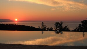 A sunset over a calm body of water with silhouettes of plants and distant land.