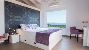 A modern bedroom with a large bed, a view of the sea, and a small desk with a chair.