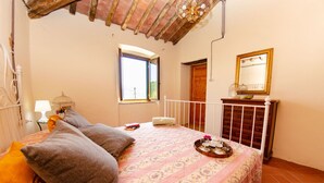 A bedroom with a bed, pillows, a bedside table with a lamp, a window, a dresser, and a mirror. - Home on the hills overlooking Pescia, between Lucca and Florence, private pool with salted water (Lanciole)