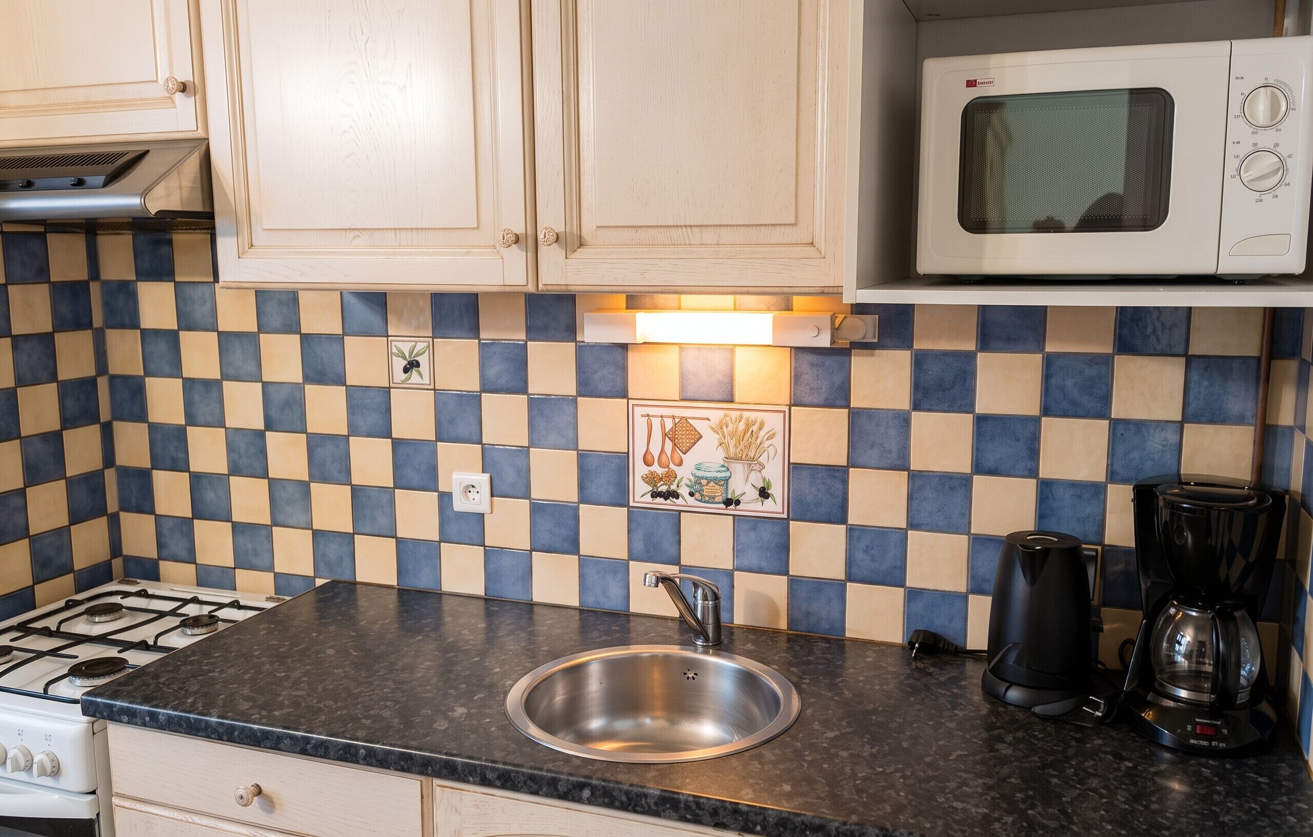 A kitchen with a checkered backsplash, a stainless steel sink, a gas stove, a microwave, and a coffee maker.