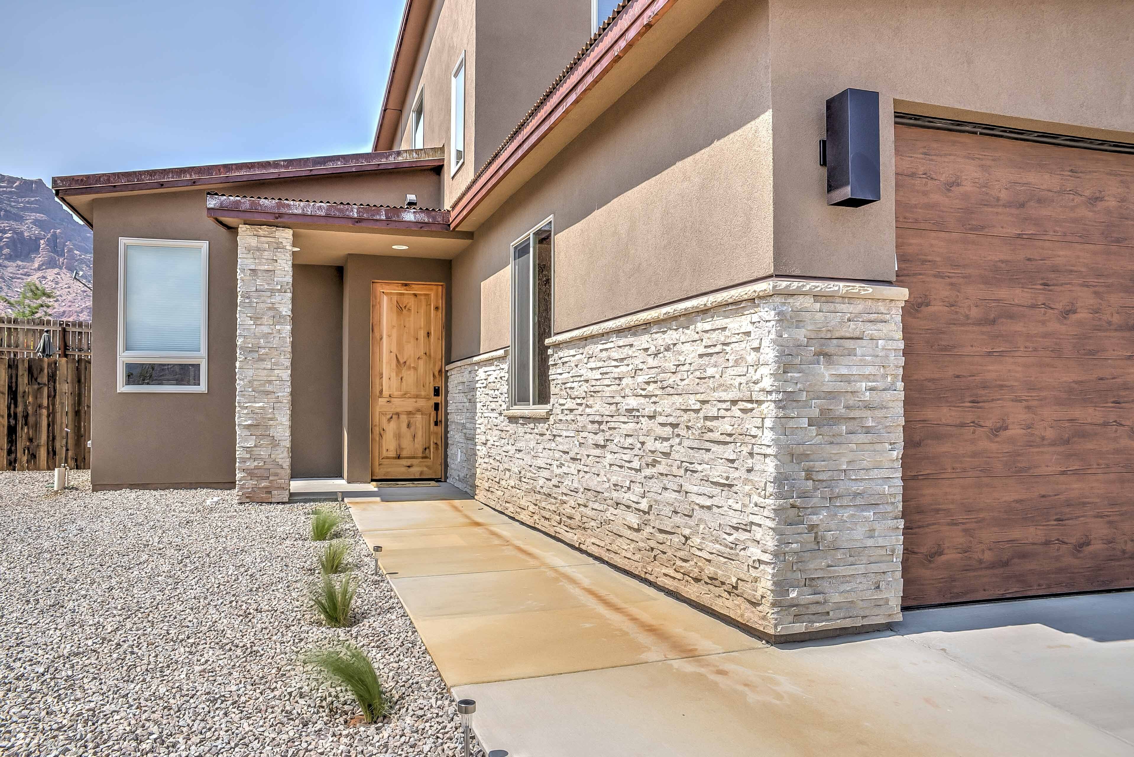 A modern house with a stone facade, a wooden door, and a concrete pathway leading to the entrance.