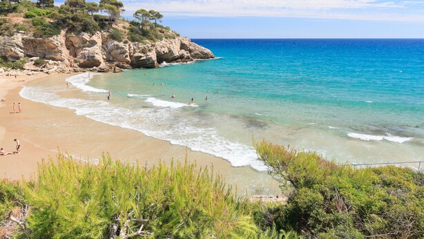 Una playa con aguas turquesas cristalinas, acantilados rocosos y vegetación verde.