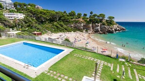 Zona de piscina con vista despejada a la playa y al océano, rodeada de vegetación y acantilados rocosos.
