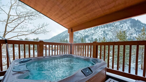 A hot tub on a wooden deck with a view of snow-covered mountains.