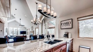 A modern kitchen with a large island, a chandelier, and a view of the outdoors.