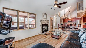 A spacious living room with a fireplace, large windows, a dining area, and a kitchen.