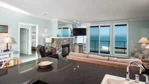 A spacious living area with a stone fireplace, a large TV, and a view of the ocean through floor-to-ceiling windows. - Promo! Stunning Oceanfront Condo, Wifi, HDTV, Hot Tub, Indoor Pool and More! (Depoe Bay)