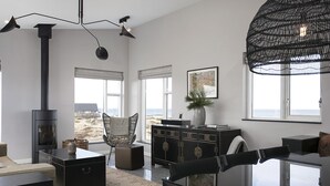 A modern living room with a fireplace, large windows, a dining area, and a view of the beach.