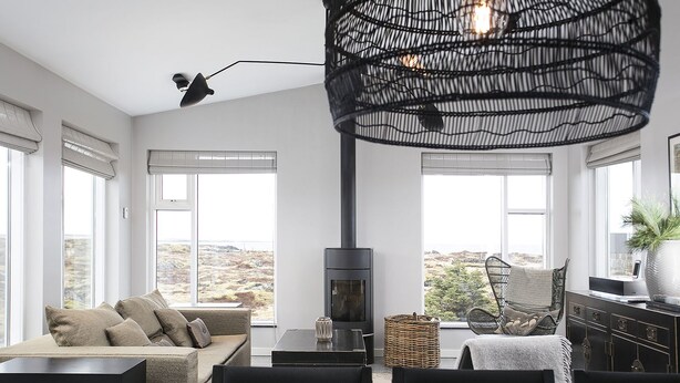 A modern living room with a sofa, dining table, chairs, a fireplace, and large windows offering a view of the outdoors.