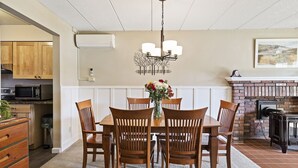 A dining area with a wooden table and chairs, a chandelier, a fireplace, and a kitchen in the background. - Ski-in/Ski-out Lodge Condo at Toll House Lift (Stowe)