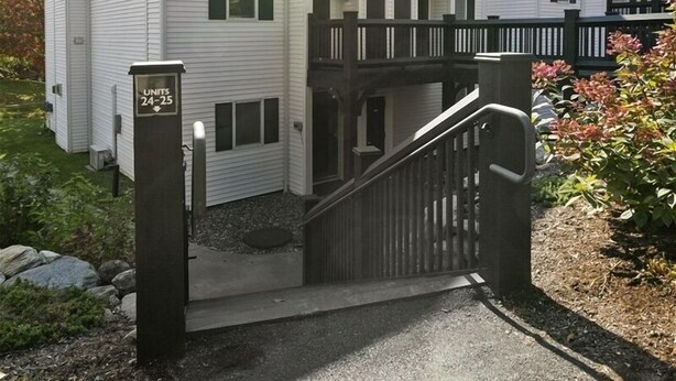 A two-story building with a gated entrance, a sign indicating unit numbers 24-25, and a small porch area. - Ski-in/Ski-out Lodge Condo at Toll House Lift (Stowe)