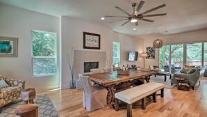Un salon spacieux avec une table à manger en bois, des sièges confortables, de grandes fenêtres et un ventilateur de plafond.