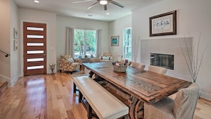 Un coin repas avec une table en bois, des bancs et des chaises. On y trouve également un ventilateur de plafond, une cheminée et une fenêtre avec des rideaux.