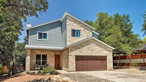 Une maison à deux étages avec une façade en pierre, un garage et un jardin aménagé à l’avant.