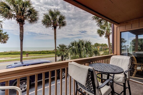 A balcony with a view of the beach, palm trees, and a car parked outside.