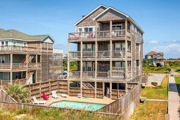 A multi-story wooden building with balconies, a swimming pool, and a deck area with lounge chairs. - Oceanfront Dog Friendly Home in Hatteras w/ Pool, Hot Tub, Elevator, Game Room (Hatteras)