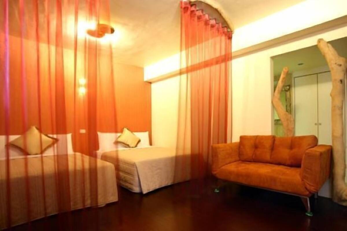 A hotel room with two beds, a sofa, and a large window with curtains.