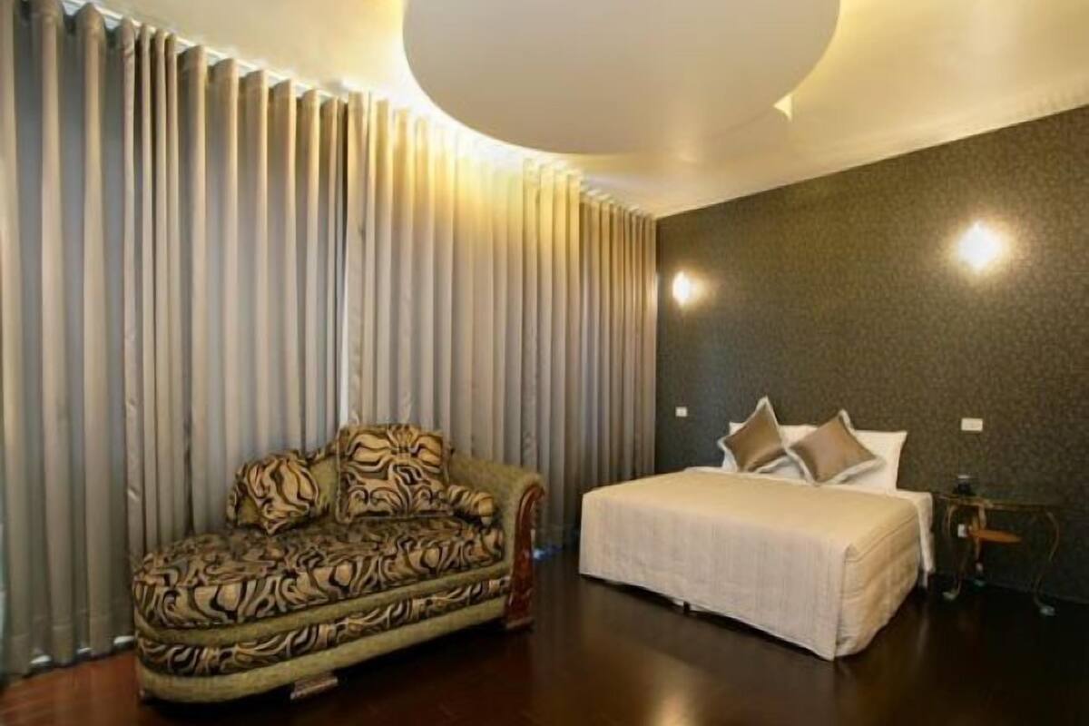 A bedroom with a patterned sofa, a bed with pillows, and a small table.