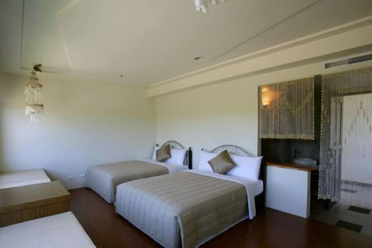 A hotel room with two beds, a small desk, and a window.