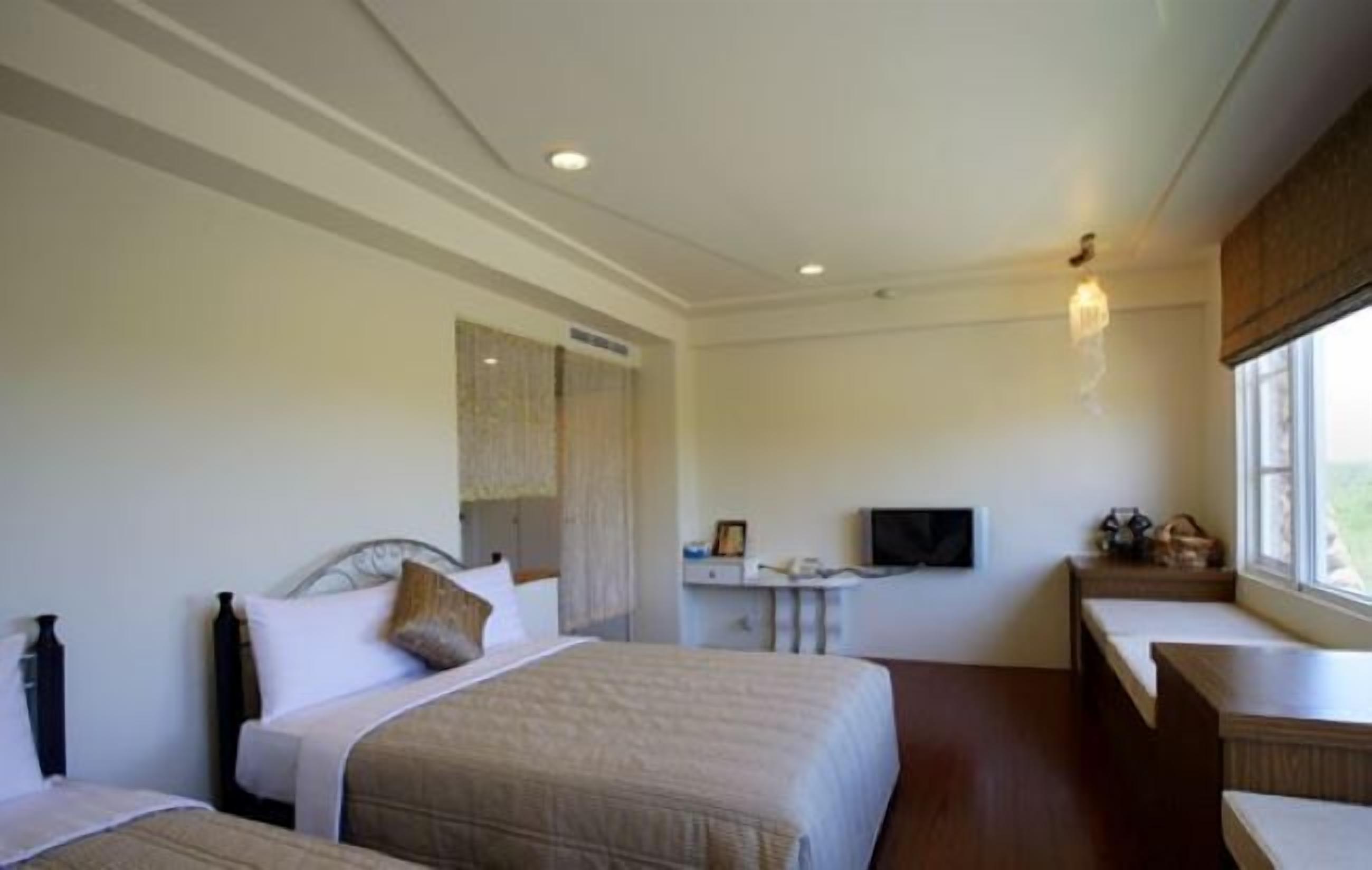 A hotel room with two beds, a desk, a television, and a window with a view.