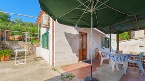 A covered outdoor patio with a table and chairs, a small garden area, and a building with a door and windows.