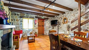 A rustic dining area with stone walls, wooden beams, a fireplace, and a television mounted on the wall.