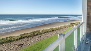 Uitzicht op een strand vanaf een balkon met een balustrade, een gazon en een kiezelstrand.