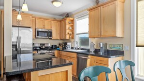 Een moderne keuken met houten kastjes, roestvrijstalen apparatuur, een granieten aanrechtblad en teal stoelen.