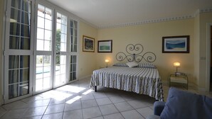 Ein Schlafzimmer mit Bett, Sessel, Nachttisch und einer großen Schiebeglastür, die zu einem Außenbereich führt.