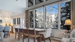 A modern kitchen with white cabinets and a dining area with a large window overlooking a snowy landscape. - Vail Village + Private Hot Tub, Game Room & Prestigious Forest Road Location (Vail)