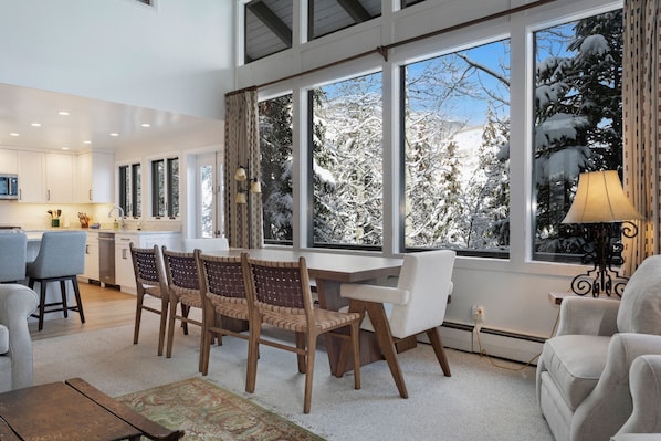 A modern kitchen with white cabinets and a dining area with a large window overlooking a snowy landscape.