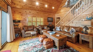 A log cabin interior with leather sofas, a wooden coffee table, and a staircase. - Brook Haven: Private Cabin, Great Views, Hot Tub, WiFi, Fireplace (Ferguson)