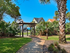 Stroll through the serene garden pathway to a charming gazebo surrounded by lush greenery and palm trees.