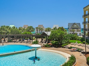 A pool area with a water fountain, lounge chairs, and a view of the ocean.