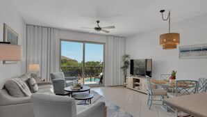Ein modernes Wohnzimmer mit Sofa, Sesseln, Couchtisch, Fernseher und Essbereich mit Stühlen und Tisch.