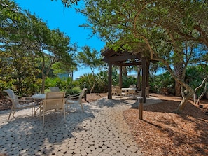 Relax in a serene outdoor space surrounded by lush greenery and a pergola, perfect for dining or unwinding.
