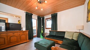 A living room with a wooden ceiling, a green sofa, a wooden cabinet, and a television. - BUDGET Chalet Alpine - Apartment B (Zell am See)