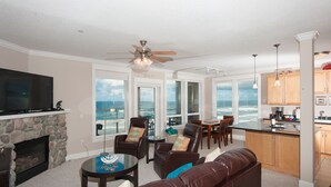 A living room with a stone fireplace, leather furniture, a television, and a view of the ocean. - Promo! Third Floor Corner Condo, Oceanfront, Private Hot Tub, Pool, Free Wifi! (Lincoln City)