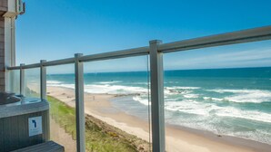 A beach view from a balcony with a metal railing, a hot tub, and a sign indicating a beach access point. - Promo! Third Floor Corner Condo, Oceanfront, Private Hot Tub, Pool, Free Wifi! (Lincoln City)