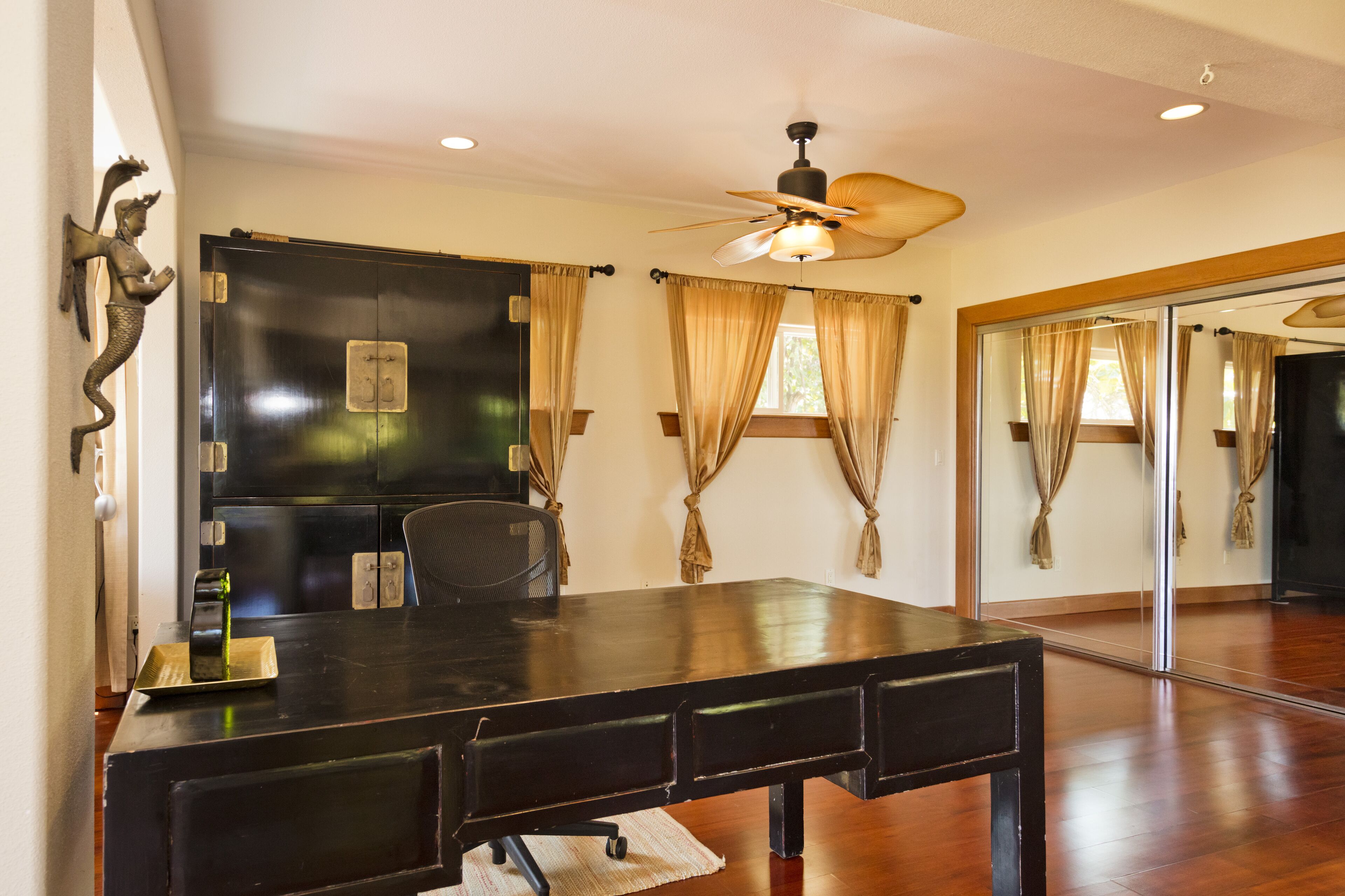 A conference room with a large table, a ceiling fan, and a mirror reflecting the room.