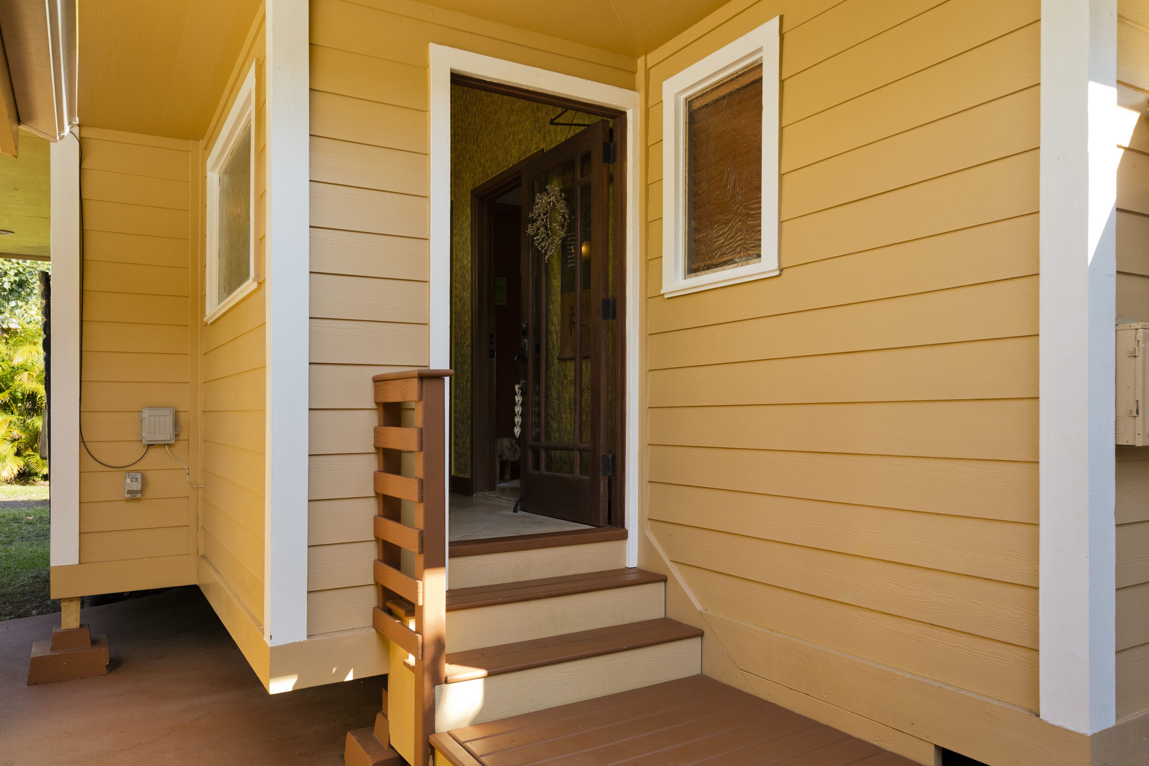 A yellow house with a wooden staircase leading to a door, a window on the side, and a small porch area.