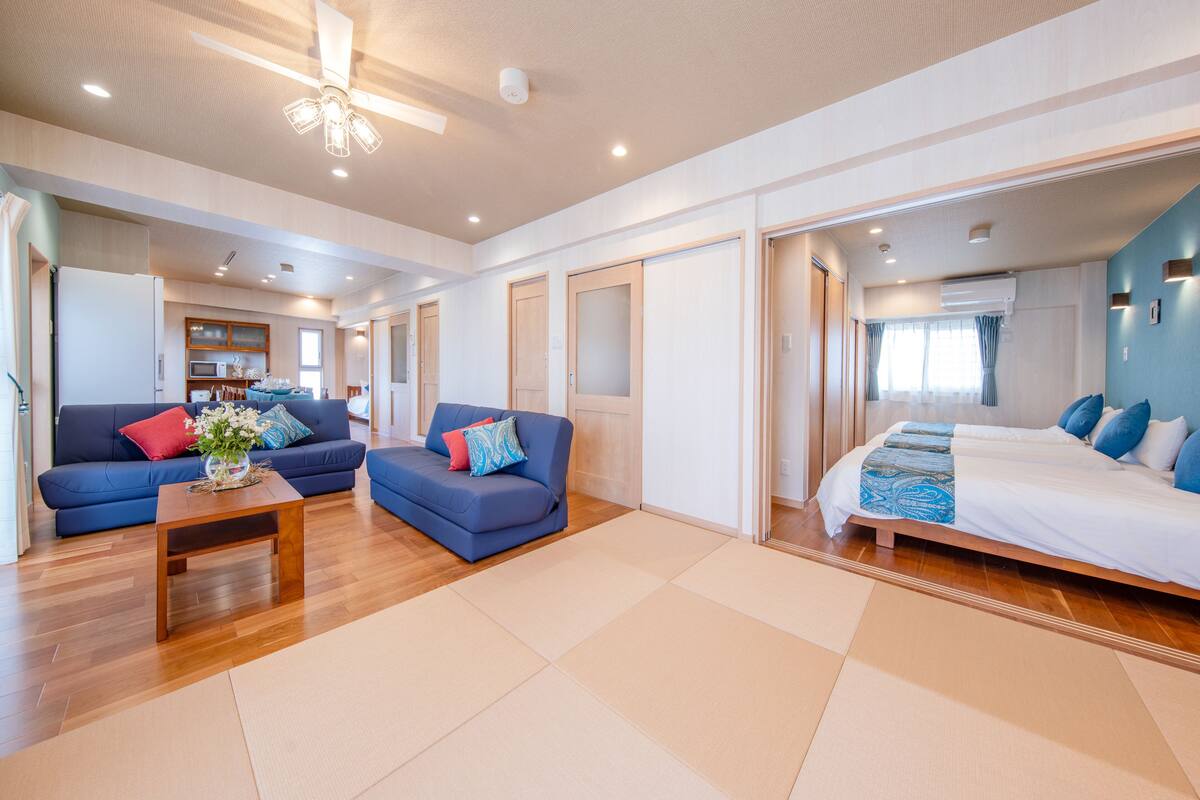 A spacious living area with a sofa, a coffee table, and a bed with a blue bedspread.