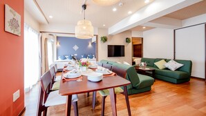 Ein modernes Wohnzimmer mit Essbereich, einem grünen Sofa, Holzböden und einem an der Wand befestigten Fernseher.