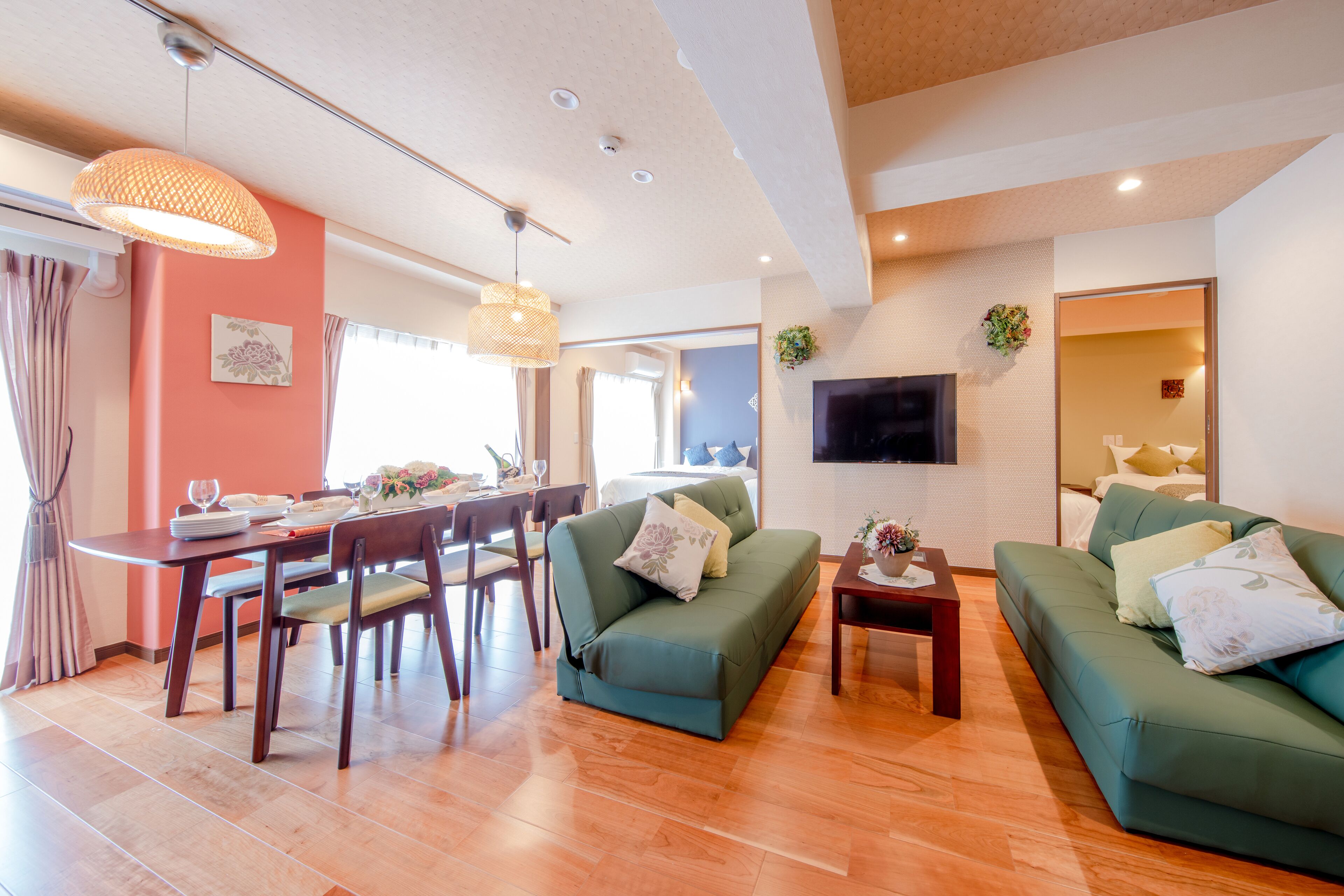 A modern living room with green sofas, a dining table with chairs, and a TV mounted on the wall.
