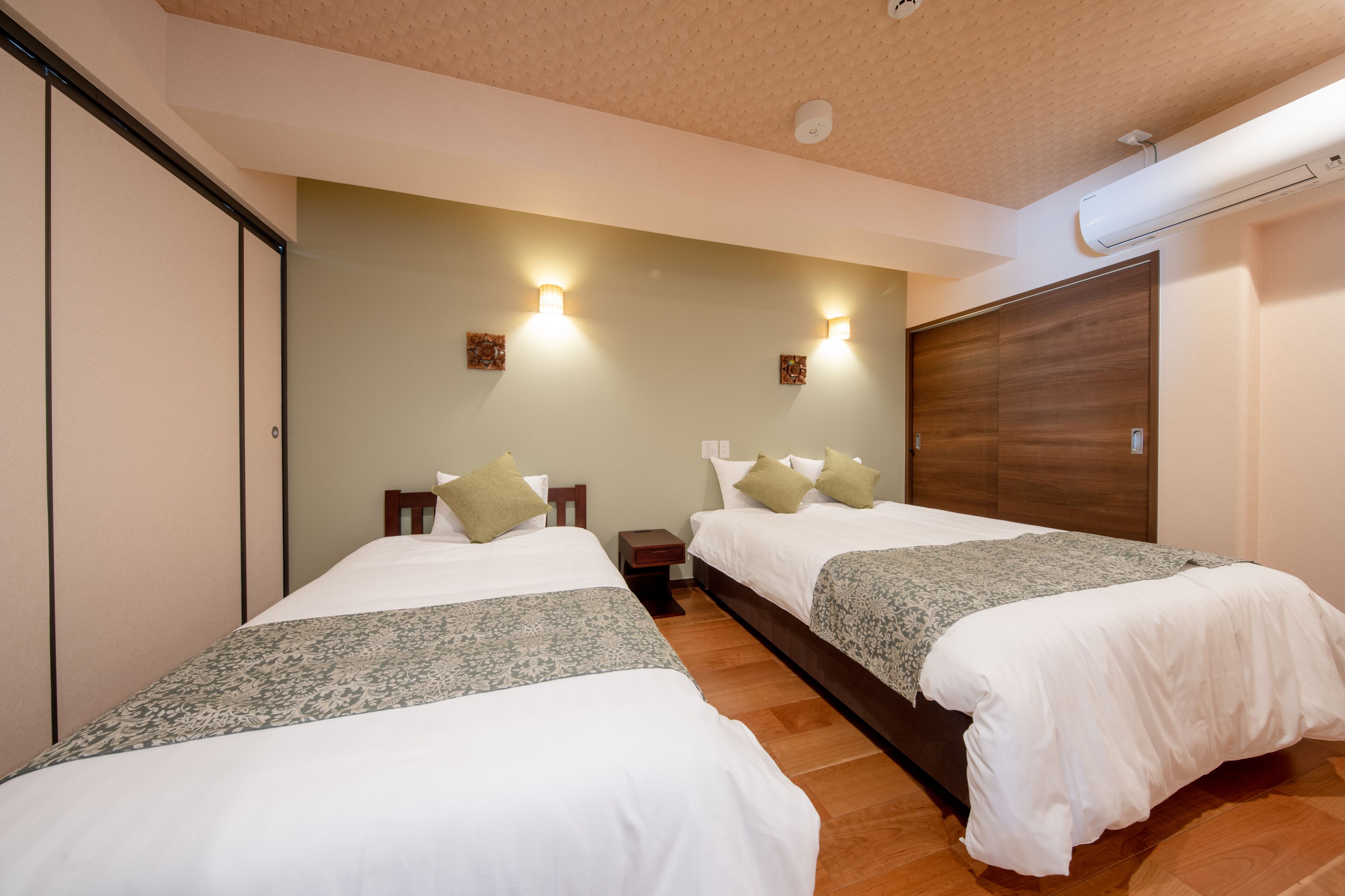 Een hotelkamer met twee bedden, een houten garderobe, een klein nachtkastje en een wandairconditioner.